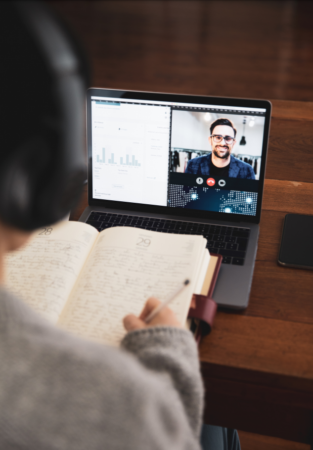 person writing in a book while video chatting on a laptop