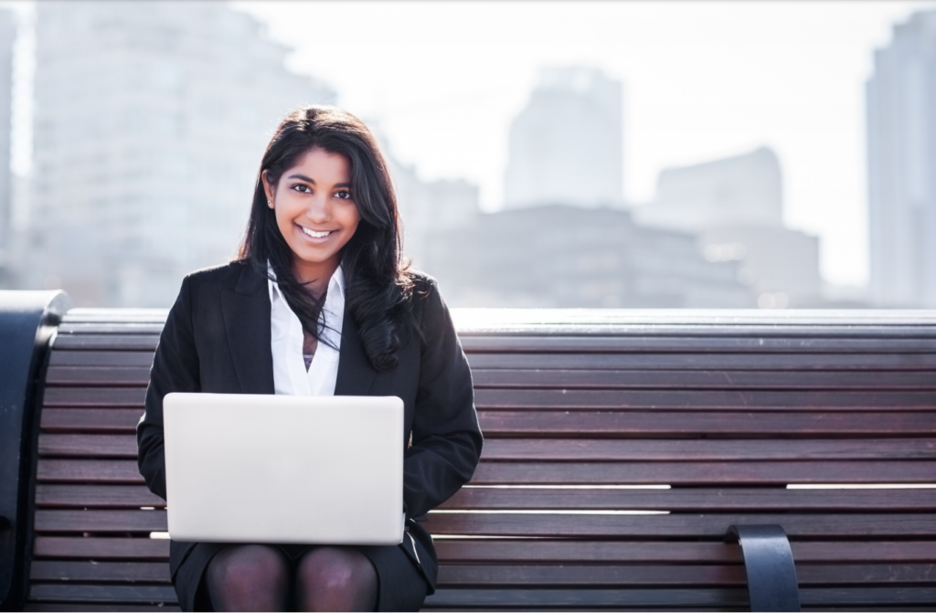 Girl smiling while sitting on a bench with a laptop on her lap