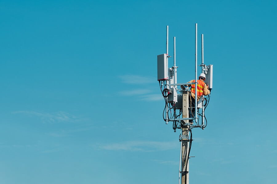 Man working on a telecoms antenna at height with blue sky behind