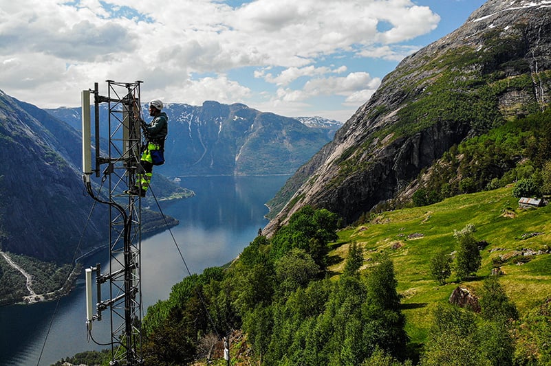 Telecoms engineer working on an antenna at height with lake and mountains behind