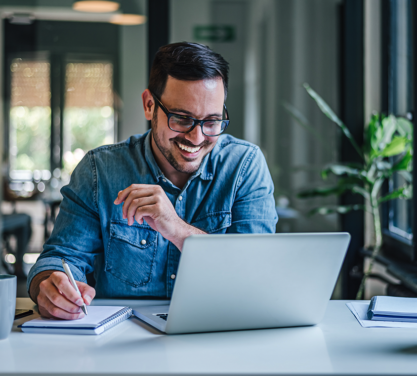 Man smiling while watching Mprical training on his laptop while taking notes