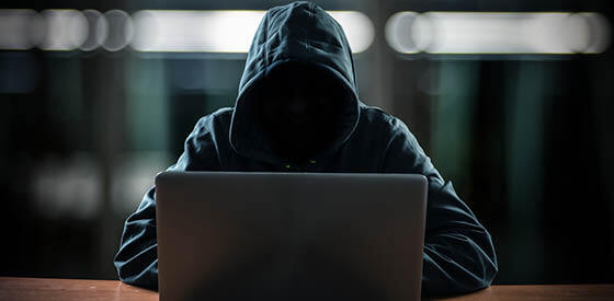 hooded figure without a face at a laptop
