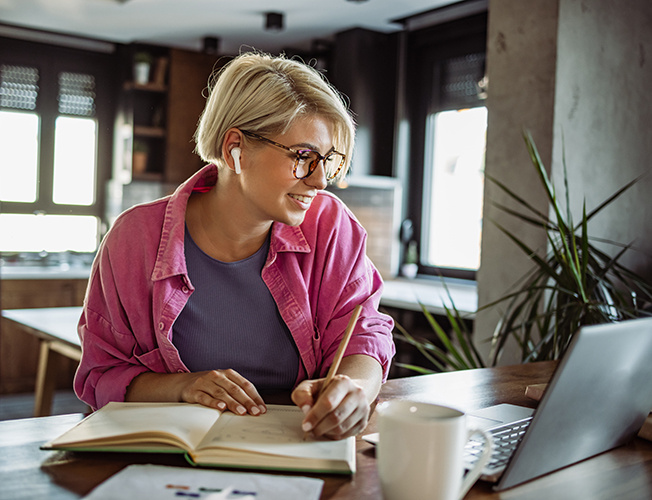 Woman writing in a notebook while viewing an Mpirical learning path on her laptop